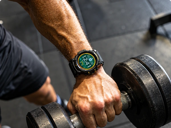 Man wearing a Hard Hat smartwatch while lifting a dumbbell at the gym, watch display showing the time.